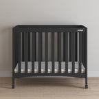 Ebony crib with a white mattress on a wooden floor against a plain wall